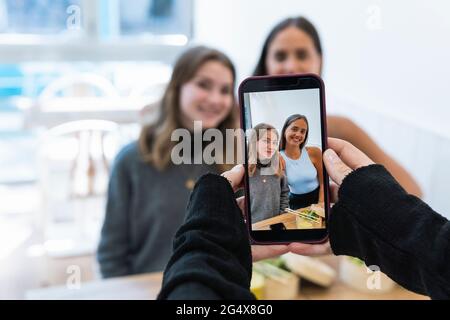 Uomo maturo che fotografa le amiche attraverso il telefono cellulare al ristorante Foto Stock