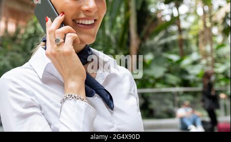 Sorridente assistente di volo femminile che parla su smartphone in giardino Foto Stock