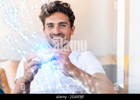 Uomo d'affari sorridente che tiene un oggetto con connessione di rete in ufficio Foto Stock