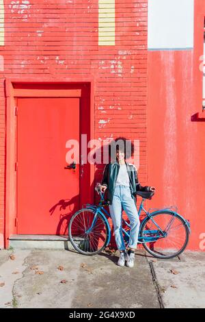 Giovane donna sorridente appoggiata in bicicletta davanti all'edificio rosso Foto Stock