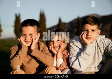 Sorridi fratelli e sorelle seduti con la mano sul mento durante il giorno di sole Foto Stock