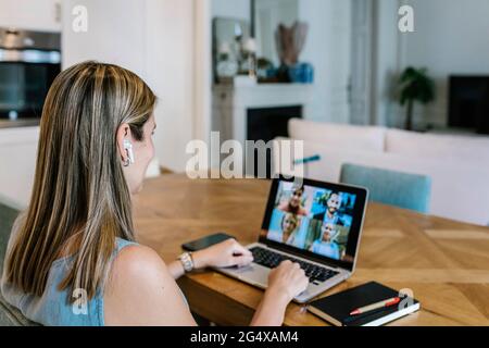 Lavoratore freelance femminile che indossa auricolari wireless che parlano in videoconferenza attraverso un computer portatile a casa Foto Stock