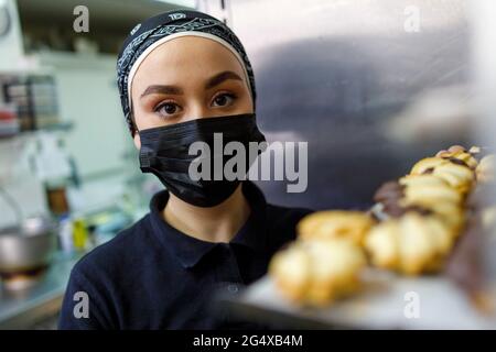 Donna che indossa una maschera protettiva in panetteria Foto Stock