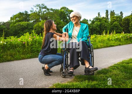 Nipote sorridente che parla con la nonna seduto in sedia a rotelle al parco Foto Stock