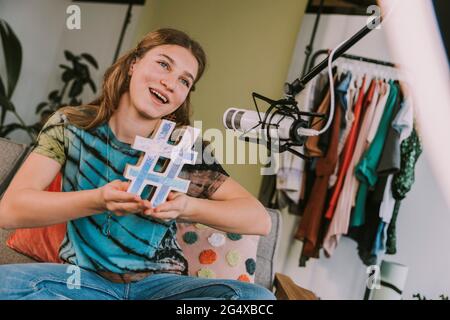 Influencer femminile che tiene il simbolo hashtag mentre vlogging a casa Foto Stock