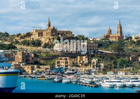 Barche ormeggiate in mare dalla chiesa parrocchiale di ghajnsielem in città il giorno soleggiato Gozo, Malta Foto Stock