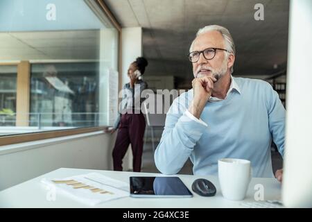 Uomo d'affari premuroso con la mano sul mento mentre la collega parla in background Foto Stock