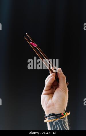 Uomo che tiene la pillola con i chopsticks su sfondo nero Foto Stock