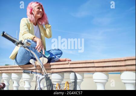 Giovane donna allegra che guarda via mentre si siede sulla ringhiera Foto Stock