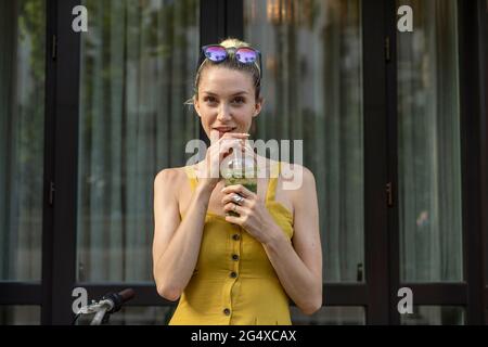 Giovane donna che beve frullato mentre si trova davanti alla porta Foto Stock