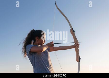 Donna che pratica tiro con l'arco dal cielo limpido Foto Stock