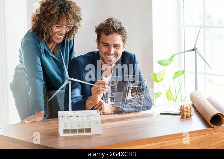 Colleghi in ufficio che guardano a uno schermo futuristico con il piano architettonico delle turbine eoliche e delle case sostenibili Foto Stock