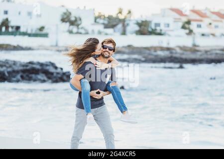 Donna che baciano l'uomo mentre piggybacking sulla spiaggia Foto Stock