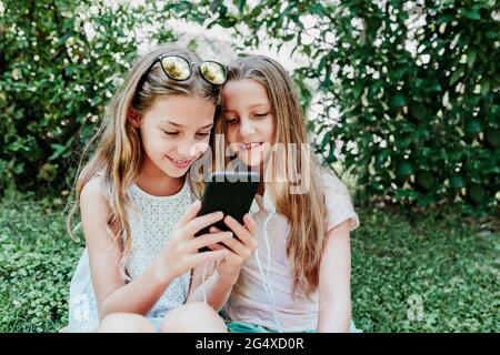 Sorridere gli amici utilizzando il telefono cellulare in giardino Foto Stock