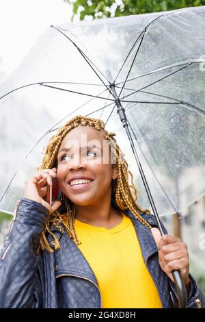 Donna sorridente che parla al telefono mentre tiene l'ombrello Foto Stock
