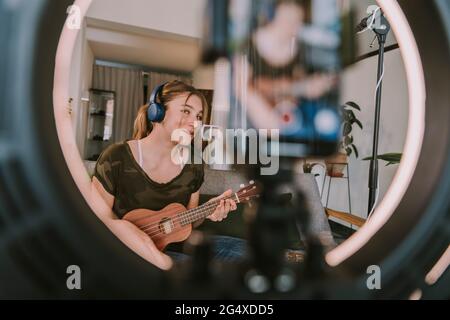 Ragazza che canta sul microfono mentre si gioca ukulele a casa Foto Stock