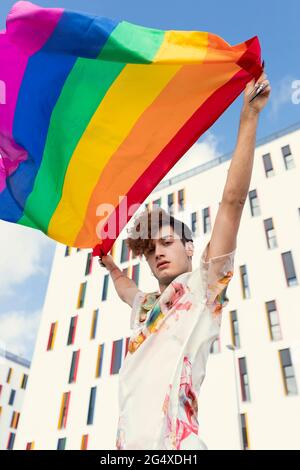 Giovane uomo che soffia bandiera arcobaleno di fronte all'edificio Foto Stock