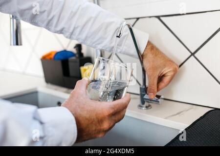 Bicchiere di riempimento professionale maschio con acqua attraverso il rubinetto a casa Foto Stock