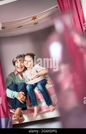 Donna anziana felice seduta con la ragazza sul letto a casa Foto Stock