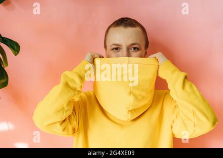 Giovane donna che ricopre la bocca con cappuccio giallo Foto Stock