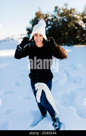 Donna sorridente che indossa un cappello a maglia godendosi nella neve Foto Stock
