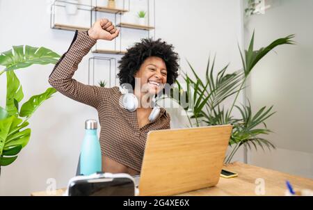 Allegra donna professionista che indossa le cuffie seduto con il computer portatile alla scrivania in ufficio Foto Stock