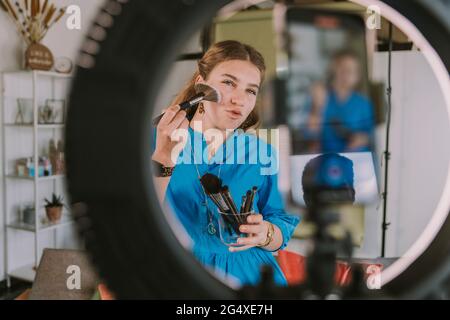 Influencer femminile che usa il pennello make-up mentre vlogging a casa Foto Stock