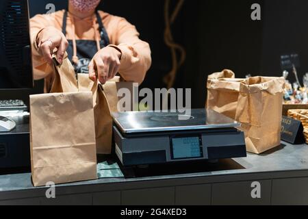 Donna proprietario del negozio che tiene borsa della spesa per peso scala sul banco Foto Stock