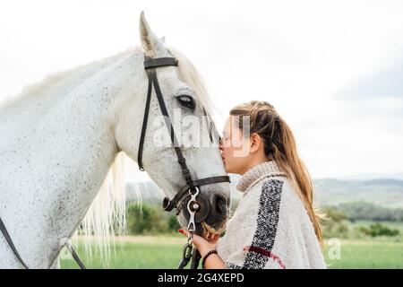 Giovane donna che bacia il cavallo bianco in campagna Foto Stock