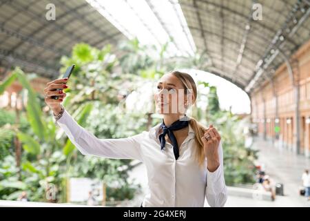 Sorridente assistente di volo che prende selfie sul telefono cellulare in giardino Foto Stock