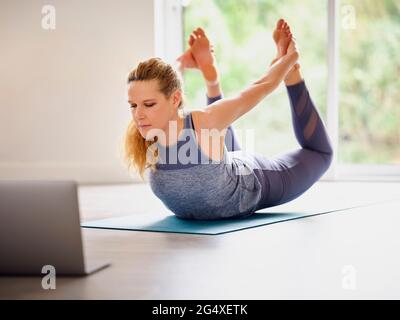 Donna matura che fa Dhanurasana a casa Foto Stock