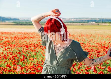 Giovane donna con balli alzati a mano su campo di papavero durante il giorno di sole Foto Stock