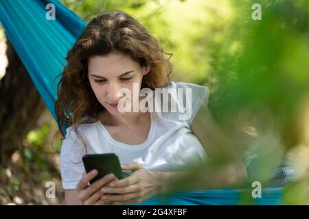 Giovane donna che usa lo smartphone mentre si rilassa sull'amaca Foto Stock