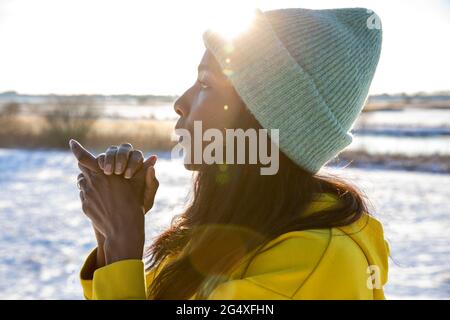 Donna matura che soffia sulle mani mentre si guarda via durante l'inverno Foto Stock