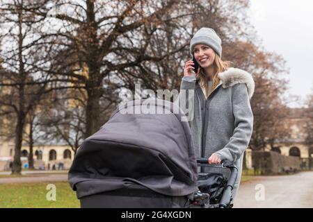 Donna sorridente che parla sul telefono cellulare mentre cammina con il passeggino Foto Stock