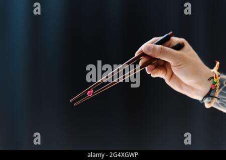 Uomo che tiene la capsula con le bacchette su sfondo nero Foto Stock