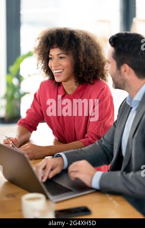 Sorridenti professionisti maschili e femminili che discutono al tavolo in ufficio Foto Stock