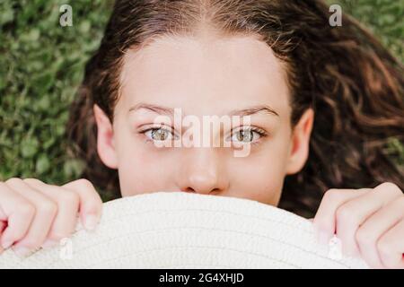 Ragazza che tiene il cappello mentre si sdraiava sull'erba in estate Foto Stock