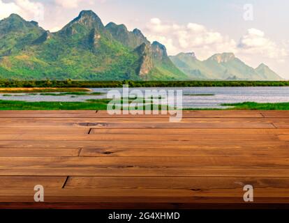 Bella tavola marrone in legno o piano di lavoro, piccola superficie lucida, vista in prospettiva, lo sfondo di un paesaggio sfocato di cielo, lago e mountè Foto Stock