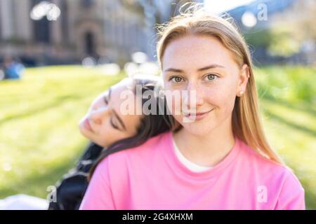 Bella donna bionda con testa sulla spalla di femmina amica in parco pubblico Foto Stock