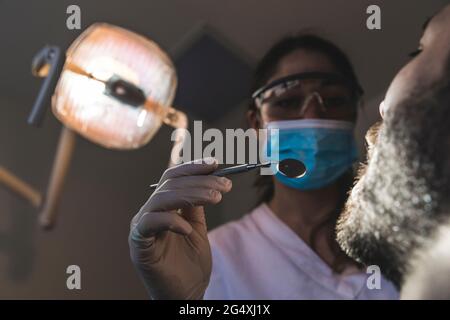 Dentista femminile che tiene lo specchio angolato presso la clinica medica Foto Stock