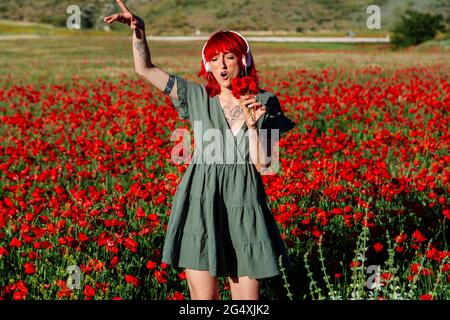 Giovane donna che tiene mazzo di fiori mentre canta su campo papavero Foto Stock