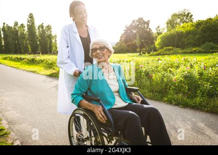 Donna di carriera con donna anziana in sedia a rotelle nel parco Foto Stock