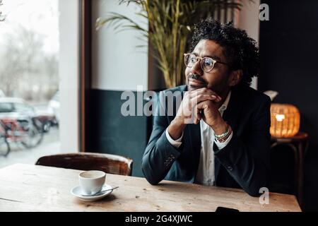 Uomo d'affari premuroso con la mano sul mento seduto in un caffè che guarda via Foto Stock