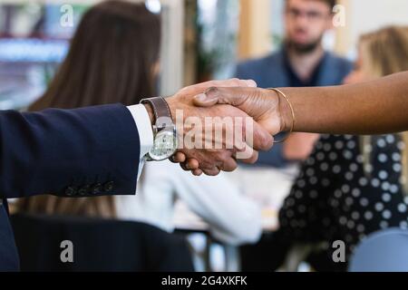 Professionisti maschili e femminili che fanno stretta di mano con i colleghi in riunione all'ufficio Foto Stock