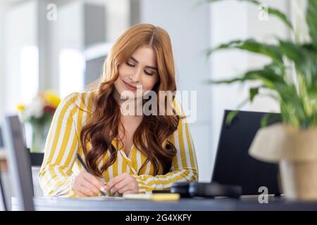 Redhead donna freelance scrittura mentre lavora da casa Foto Stock