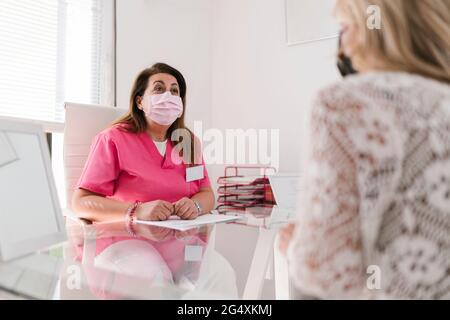 Donna estetista in maschera protettiva del viso discutere con la donna in clinica Foto Stock