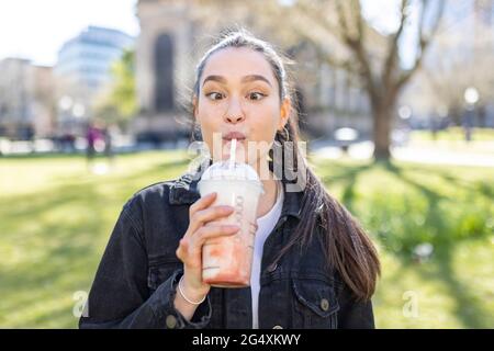 Giovane donna che guarda gli occhi incrociati mentre beve il milkshake al parco Foto Stock