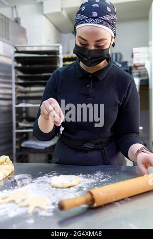 Panettiere femminile che spruzzano la farina mentre si arrotola l'impasto al forno Foto Stock