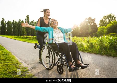 Felice nipote che spinge la nonna seduto in sedia a rotelle al parco Foto Stock